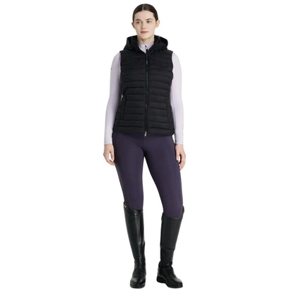 Eine Reiterin im kompletten LeMieux Reitoutfit bereit für den Sattel. Die schwarze LeMieux Steppweste Rose wird hier stilvoll kombiniert und zeigt sich als vielseitiges Essential für den Reitsport. Das Bild vermittelt die perfekte Passform und Eleganz der Pufferweste in Aktion am Pferd. Hochwertige Reiterbekleidung für Damen, die Funktionalität im Stall mit einem modernen Look verbindet. Ideal als Inspiration für ein abgestimmtes Outfit im klassischen LeMieux-Stil.