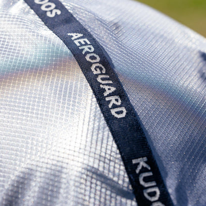 Nahaufnahme des markanten Kudos AeroGuard Logos auf dem robusten Topband der LeMieux Fliegendecke. Darunter entfaltet das hochtechnische, silberne Ripshield-Mesh-Grundmaterial seine perlmuttartig schimmernde und lichtreflektierende Wirkung für optimalen Hitzeschutz im Sommer.