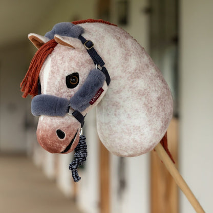 Hobby Horse Poppy von LeMieux in einer Stallgasse. Die Rotschimmel-Stute trägt ein blaues Halfter mit Plüschpolstern und zeigt eine schmale weiße Blesse auf dem Nasenrücken.