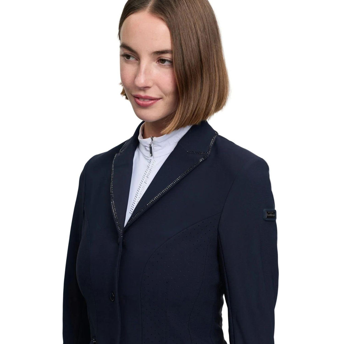 Detailansicht des LeMieux Damen-Turnierjackets Brilliance Diana in Navy, das eine Reiterin über einem weißen Turniershirt zeigt, mit Nahaufnahme der zweireihigen Glitzersteine am Reverskragen, feinen perforierten Belüftungseinsätzen sowie dem LeMieux-Markenlogo am Ärmel für eine elegante Silhouette im Turniersport.