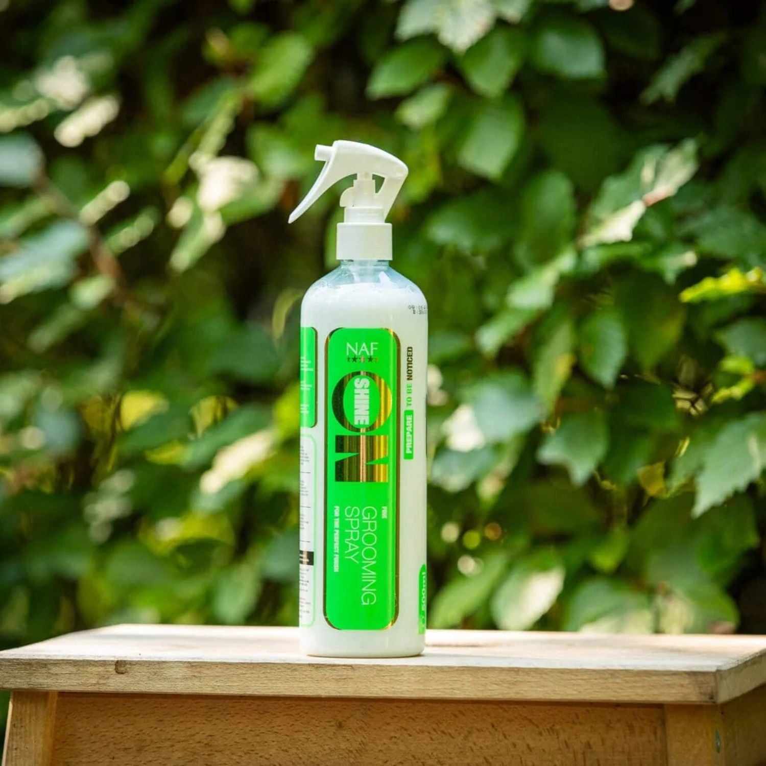 NAF Shine On Glanzspray für Pferde – Produktflasche draußen auf dem Hof, Premium Fellpflege für Mähne, Schweif &amp; glänzendes Pferdefell im Sonnenlicht