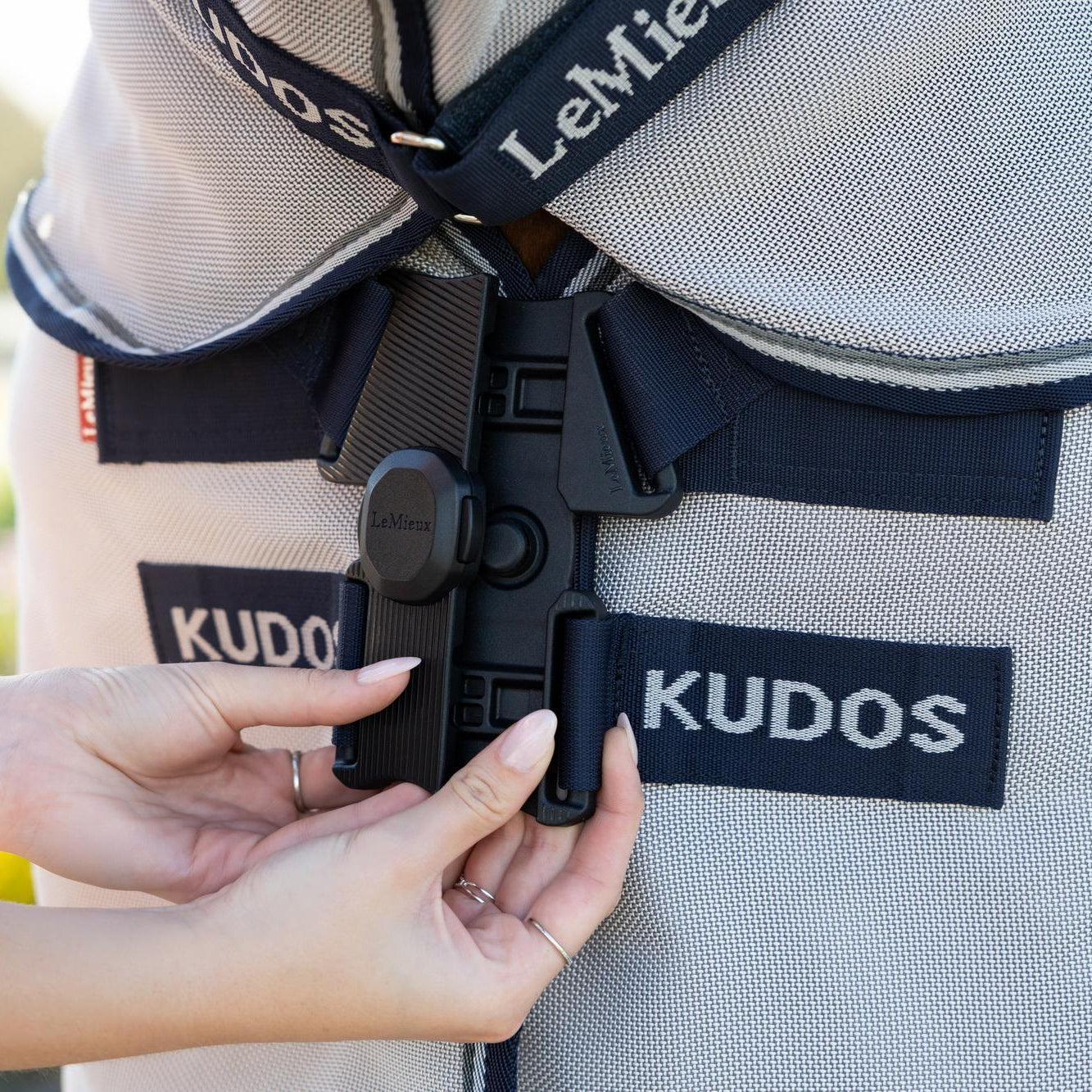 Eine Reiterin verschließt den innovativen LeMieux Neo-Lock-Verschluss der Kudos Gladiator Fliegenschutzdecke mit den Händen und demonstriert anschaulich, wie die beiden Verschlussseiten durch das clevere Design perfekt ineinandergreifen.