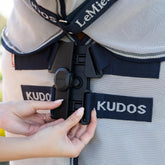 Eine Reiterin verschließt den innovativen LeMieux Neo-Lock-Verschluss der Kudos Gladiator Fliegenschutzdecke mit den Händen und demonstriert anschaulich, wie die beiden Verschlussseiten durch das clevere Design perfekt ineinandergreifen.