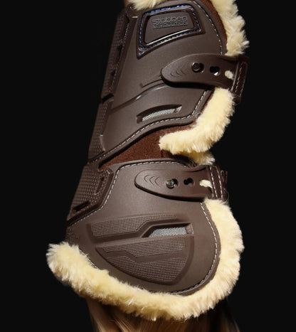 Nahaufnahme der braunen Stübben Evolution Hybrid Gamasche von der Seite: Die stoßabsorbierende TPE-Hartschale schützt die Beugesehne zuverlässig vor Tritten. Gut erkennbar ist die ergonomische Aussparung für maximale Fesselgelenks-Freiheit sowie die vertikalen Belüftungskanäle zur Thermoregulation. Die elastischen Schnellverschlüsse mit stabilen Pin-Knöpfen garantieren eine individuelle Passform und verhindern störende Druckpunkte am Pferdebein während der Springgymnastik.