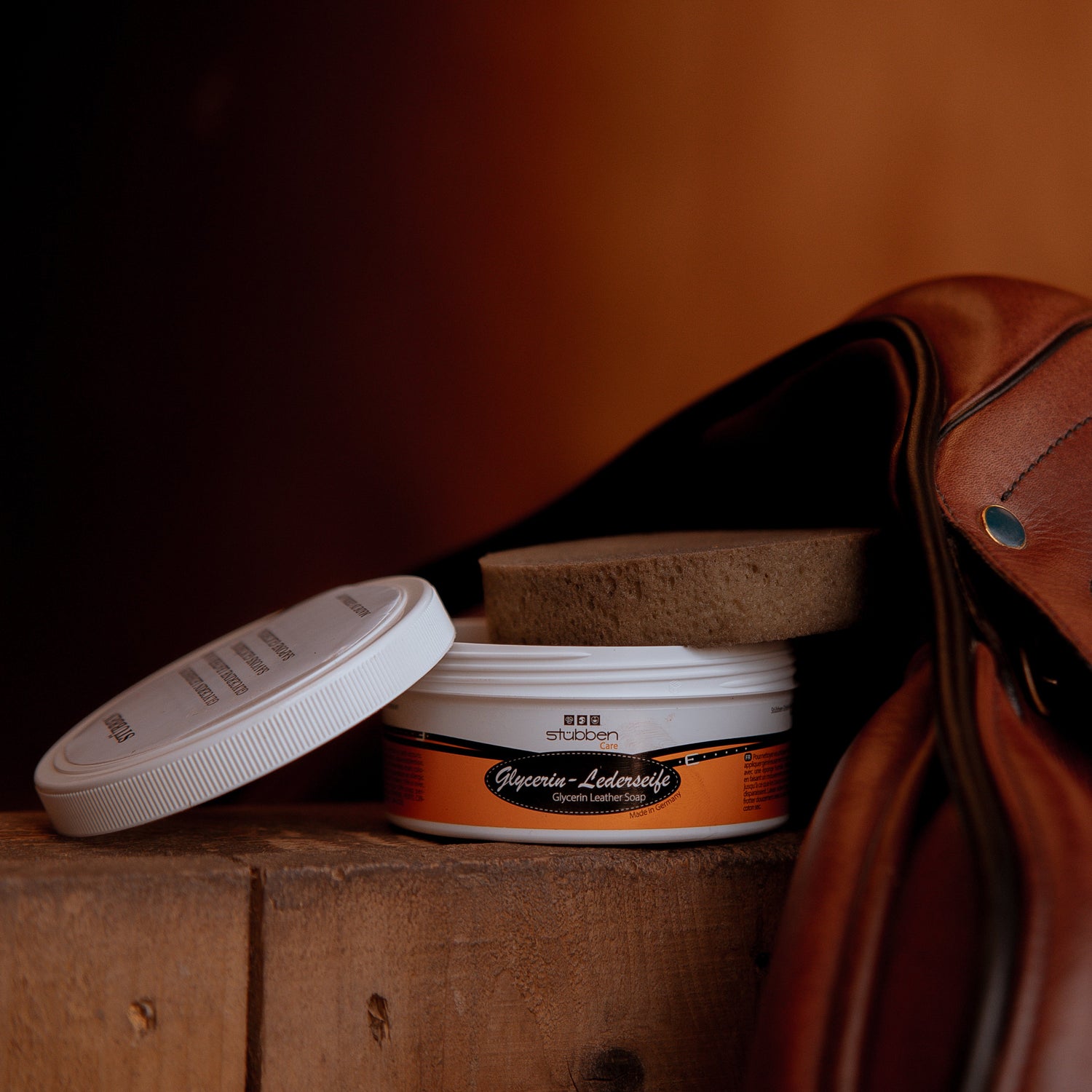 Ein gebrauchter Schwamm liegt auf der 250 g Dose Stübben Glycerin Sattelseife vor dem Vorderzwiesel eines braunen Stübben Sattels und verdeutlicht die effektive Schmutzentfernung bei der Reinigung von hochwertigem Glattleder.