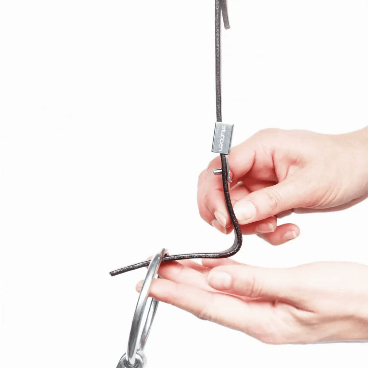 Detailaufnahme der Funktionsweise des Stübben Slide&amp;Lock-Systems an der Stübben-Trense: Eine Hand schiebt die silberne Metallabdeckung, den Slider nach oben, um den Dorn am Backenstück freizugeben und den Gebissring für einen schnellen, werkzeuglosen Gebisswechsel mit nur einem Handgriff auszutauschen.