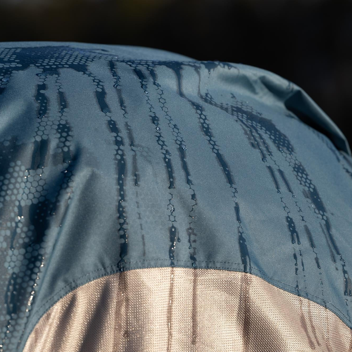 Eine weitere Detailaufnahme veranschaulicht den Trocknungsprozess des wasserreaktiven Ripstop-Materials der LeMieux Hybriddecke, bei dem der dunkle Camouflage-Print langsam verschwindet und dem Stoff wieder seine einheitliche Farbe zurückgibt.