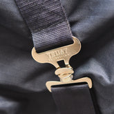Diese Detailaufnahme zeigt die stabilen, metallischen T-Verschlüsse der gekreuzten Bauchgurte mit der exklusiven Trust Equestrian Aufschrift, die für eine sichere Fixierung der 100g Outdoordecke sorgen und durch ihre robuste Verarbeitung eine langlebige Positionierung des Tetris-Systems am Pferdekörper garantieren.