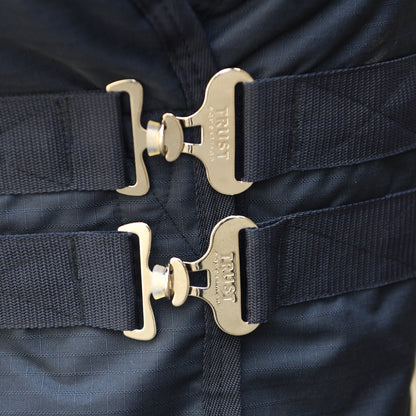 Die Detailaufnahme zeigt den stabilen Brustverschluss der Trust Equestrian Tetris Outdoordecke mit zwei robusten, metallischen T-Haken-Verschlüssen plus Sicherheitsgummis inklusive Trust-Logo-Prägung, die für einen sicheren Halt in der Brustposition sorgen und ein Verrutschen der 100g Weidedecke verhindern.