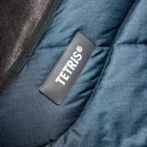 Das Bild zeigt das Logo der Deckenserie Tetris von Trust Equestrian. Das Logo ist am Halsbereich bzw. dem oberen Rand des Halsbereiches angebracht. Darunter ist das weiche und dicke Blockpolster eingearbeitet, das für Druckausgleich und eine stabile Verteilung der Kräfte sorgt. Haarbruch, Druckstellen und Scheuerstellen werden vermieden.