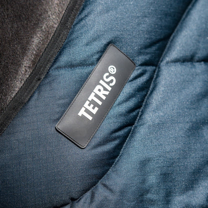 Das Bild zeigt das Logo der Deckenserie Tetris von Trust Equestrian. Das Logo ist am Halsbereich bzw. dem oberen Rand des Halsbereiches angebracht. Darunter ist das weiche und dicke Blockpolster eingearbeitet, das für Druckausgleich und eine stabile Verteilung der Kräfte sorgt. Haarbruch, Druckstellen und Scheuerstellen werden vermieden.