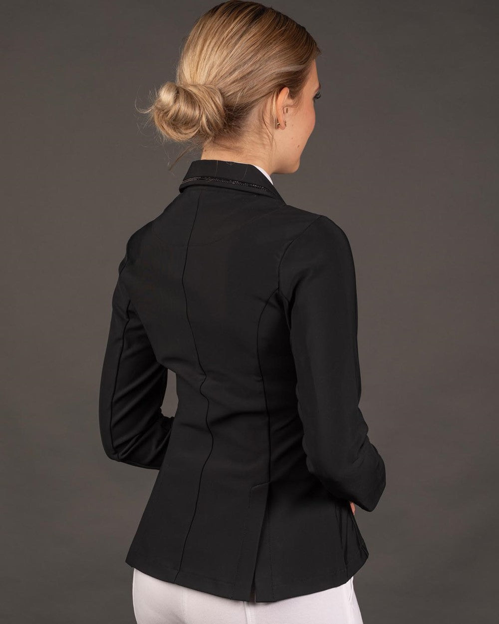 In der seitlichen Rückansicht der Reiterin wird die körpernahe Passform der eleganten Turnierbekleidung für Damen und Kinder deutlich, ideal ergänzt durch die bequemen Reitrock-Schlitze für jede Reitsportdisziplin.