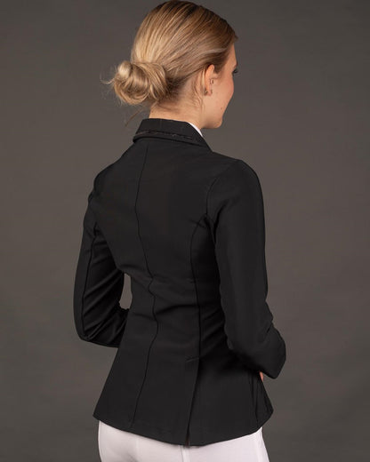 In der seitlichen Rückansicht der Reiterin wird die körpernahe Passform der eleganten Turnierbekleidung für Damen und Kinder deutlich, ideal ergänzt durch die bequemen Reitrock-Schlitze für jede Reitsportdisziplin.