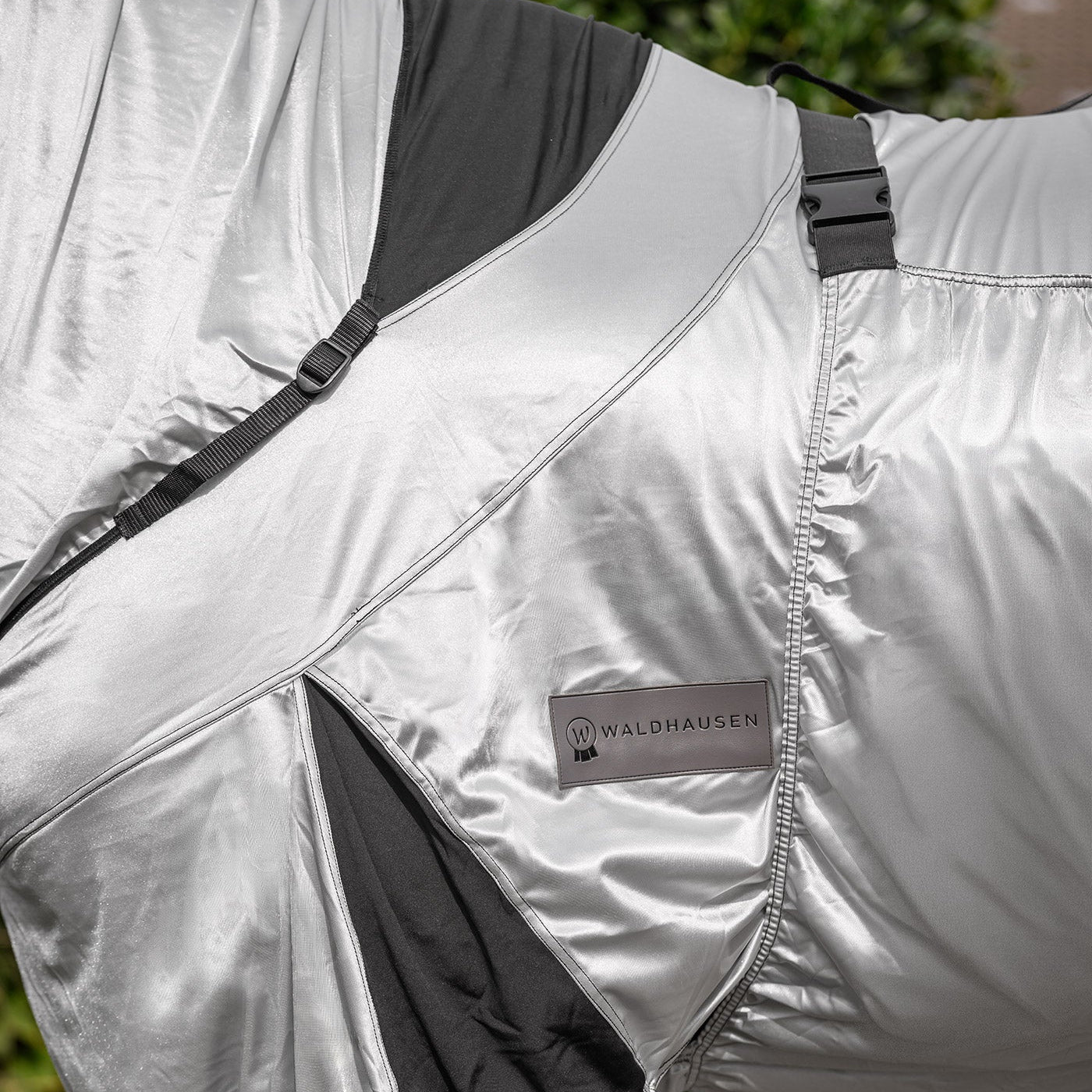 Detailaufnahme der hellen Waldhausen Ekzemerdecke Premium mit Fokus auf die dunkel abgesetzten, elastischen Einsätze im Hals- und Brustbereich sowie an der Gehfalte. Diese Elastizität bietet Ponys und Pferden auf der Weide volle Bewegungsfreiheit für das Grasen, Galoppieren, Buckeln, Wälzen und Liegen. Die individuell anpassbaren Gurte ermöglichen eine körpernahe, gute Passform dieser leichten Ekzemerdecke für den Sommer, ohne das Tier einzuschränken.