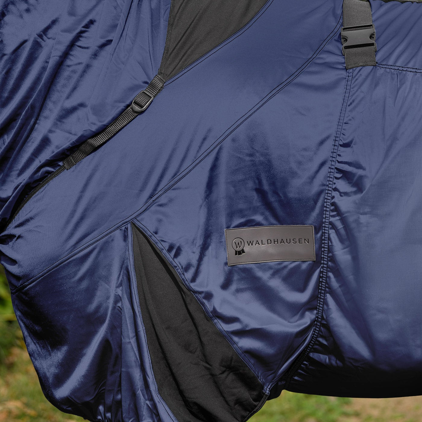 Detailaufnahme der dunkelblauen  Waldhausen Ekzemerdecke Premium mit Fokus auf die dunkel abgesetzten, elastischen Einsätze im Hals- und Brustbereich sowie an der Gehfalte. Diese Elastizität bietet Ponys und Pferden auf der Weide volle Bewegungsfreiheit für das Grasen, Galoppieren, Buckeln, Wälzen und Liegen. Die individuell anpassbaren Gurte ermöglichen eine körpernahe, gute Passform dieser leichten Ekzemerdecke für den Sommer, ohne das Tier einzuschränken.
