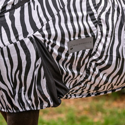 Detailaufnahme der Waldhausen Ekzemerdecke Zebra Premium in schwarz-weiß, die die dunkel abgesetzte Gehfalte und das sichtbare Waldhausen-Logo zeigt. Dieses Zebra-Design bietet Pferden und Ponys maximale Bewegungsfreiheit auf der Weide beim Galoppieren, Spielen und Buckeln. Der funktionale Zebra-Print dient als mechanischer Fliegenschutz zur Abwehr von Kriebelmücken, während die elastische Gehfalte dieser Sommerdecke eine optimale, körpernahe Passform beim Freilauf.