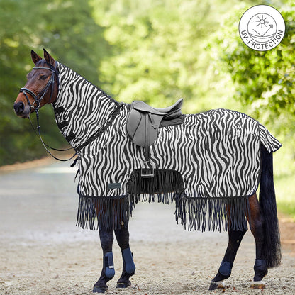 Waldhausen Fliegen-Ausreitdecke Zebra mit Fransen und eingeblendetem UV-Protection-Button am gesattelten Pferd im Gelände. Gut erkennbar ist der Materialrückschnitt im Bereich der Sattel- und Schenkellage für engen Kontakt vom Reiterbein und eine gefühlvolle Hilfengebung. Das feste Halsteil deckt den Mähnenkamm ab, während der Schweiflatz Schweifrübe und Schweifansatz schützt. Diese Reitdecke vereint optische und mechanische Fliegenabwehr für entspannte Sommer-Ritte mit dem Pferd.