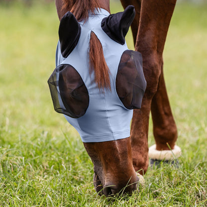 Grasendes Pferd beim Weidegang mit der hellen pastellblauen Waldhausen Fliegenmaske Puck. Der integrierte, klassische Schopfdurchlass zwischen den Ohren ermöglicht es, den Schopf nach außen zu ziehen, wodurch ein Haarestau vermieden wird. Diese leichte Fliegenschutzmaske im Sommer dient als mechanischer Fliegenschutz für Pferde und Ponys. Der neutrale, sanfte hellblaue Farbton der Weidemaske passt optisch zu vielen Fellfarben der Ponys und Pferde auf der Koppel.