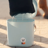 Aus dem Wassereimer gehobene Waldhausen Health + Care Ice-Layer Kühldecke in ihrer Netztasche, während überschüssiges Wasser zurück in den hellblauen Eimer (Multibag) abläuft. Durch das kurze Abtropfenlassen und anschließende Auswringen wird die Decke tropffrei vorbereitet, um dem Pferd auf dem Rücken eine gleichmäßige Verdunstungskühlung ohne lästiges Nässelaufen zu spenden.