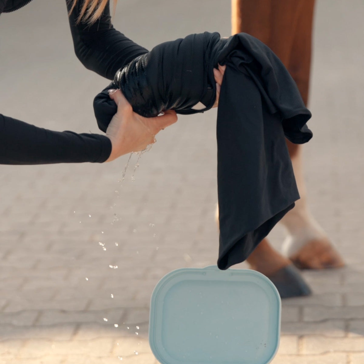Gründliches Auswringen der nassen Waldhausen Health + Care Ice-Layer Kühldecke mit beiden Händen über dem Eimer, sodass überschüssiges Wasser heraustropft. Durch diesen Handgriff wird das Funktionsmaterial optimal vorbereitet, um dem Pferd auf dem Rücken eine wohltuende Verdunstungskühlung ganz ohne lästiges Tropfen zu bieten.