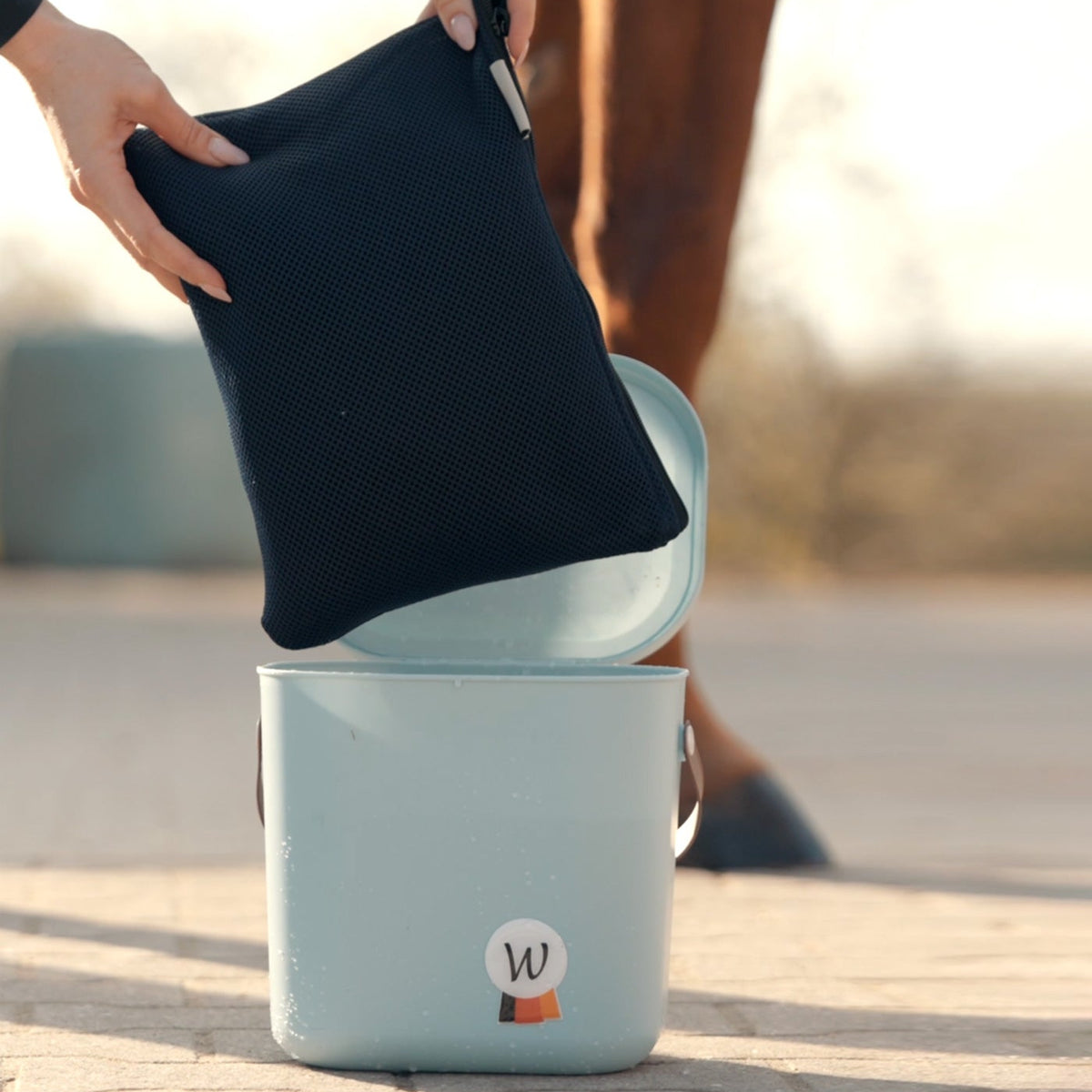 Vorbereitung der Waldhausen Health + Care Ice-Layer Kühldecke: Die zusammengefaltete Pferdedecke wird in ihrer praktischen Netztasche direkt in einen Eimer (Multibag) mit frischem Wasser getaucht, um sich vollständig vollzusaugen. Diese wassersparende Methode ermöglicht eine unkomplizierte Aktivierung der Verdunstungskühlung am Stall, auf dem Paddock oder unterwegs auf dem Turnier ganz ohne Wasserschlauch.