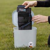 Eine Reiterin taucht die schwarze Waldhausen Health + Care Ice-Layer Kühlgamasche in die mit Wasser gefüllte Tasche Waldhausen Multibag ECO. Das Bild zeigt die einfache Vorbereitung der Gamaschen, damit sie sich komplett vollsaugen. Ohne aufwendiges Vorkühlen im Gefrierfach nutzen die Kühlgamaschen später die Verdunstungskühlung, um warme Pferdebeine nach dem Training oder bei großer Sommerhitze effektiv zu kühlen. Ideal für die Pferdepflege am Stall.