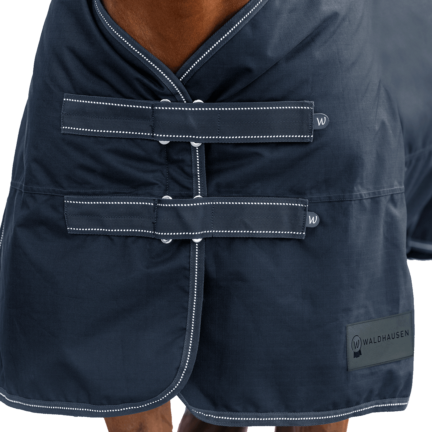 Detailaufnahme des doppelten Brustverschlusses der Waldhausen Outdoordecke Arctic 100 g in Nachtblau. Die robusten T-Verschlüsse sind mit Klettabdeckungen geschützt, und können ein Hängenbleiben im Offenstall oder Paddock reduzieren. Der doppelte Brustverschluss ermöglicht einfaches Ein- und Ausdecken von Pferd oder Pony. Reflektierende Kontrastnähte in Weiß auf den Klettlaschen und dem Einfassband erhöhen die Sichtbarkeit bei Dunkelheit.