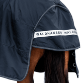 Rückansicht der dunkelblauen Waldhausen-Outdoordecke Arctic 100 g in Nachtblau mit Fokus auf den langen Schweiflatz. Der großzügige Schweiflatz schützt Schweif und Schweifrübe des Pferdes zuverlässig vor Wind, Regen und Kälte. Die breite, reflektierende Waldhausen-Applikation sorgt für optimale Sichtbarkeit von hinten im Dunkeln, auf der Weide, auf Wegen oder im Straßenverkehr. Die perfekte 600D-Ripstop-Regendecke für bessere Sichtbarkeit im Dunklen. D-Ringe für Beinschnüre sind zu sehen.