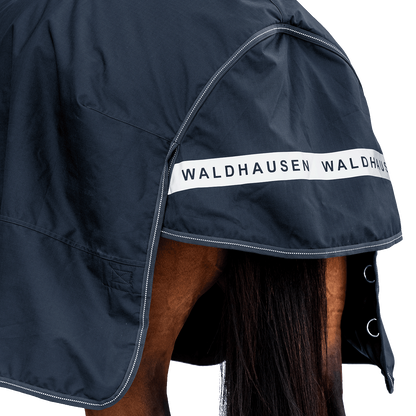 Rückansicht der dunkelblauen Waldhausen-Outdoordecke Arctic 200 g in Nachtblau mit Fokus auf den langen Schweiflatz. Der großzügige Schweiflatz schützt Schweif und Schweifrübe des Pferdes zuverlässig vor Wind, Regen und Kälte. Die breite, reflektierende Waldhausen-Applikation sorgt für optimale Sichtbarkeit von hinten im Dunkeln, auf der Weide, auf Wegen oder im Straßenverkehr. Die perfekte 600D-Ripstop-Regendecke für bessere Sichtbarkeit im Dunklen. D-Ringe für Beinschnüre sind zu sehen.