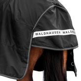 Rückansicht der dunklen Waldhausen-Outdoordecke Arctic 200 g in Schwarz mit Fokus auf den langen Schweiflatz. Der großzügige Schweiflatz schützt Schweif und Schweifrübe des Pferdes zuverlässig vor Wind, Regen und Kälte. Die breite, reflektierende Waldhausen-Applikation sorgt für optimale Sichtbarkeit von hinten im Dunkeln, auf der Weide, auf Wegen oder im Straßenverkehr. Die perfekte 600D-Ripstop-Regendecke für bessere Sichtbarkeit im Dunklen. D-Ringe für Beinschnüre sind zu sehen.