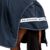 Rückansicht der dunkelblauen Waldhausen-Outdoordecke Arctic 50 g in Nachtblau mit Fokus auf den langen Schweiflatz. Der großzügige Schweiflatz schützt Schweif und Schweifrübe des Pferdes zuverlässig vor Wind, Regen und Kälte. Die breite, reflektierende Waldhausen-Applikation sorgt für optimale Sichtbarkeit von hinten im Dunkeln, auf der Weide, auf Wegen oder im Straßenverkehr. Die perfekte 600D-Ripstop-Regendecke für bessere Sichtbarkeit im Dunklen. D-Ringe für Beinschnüre sind zu sehen.