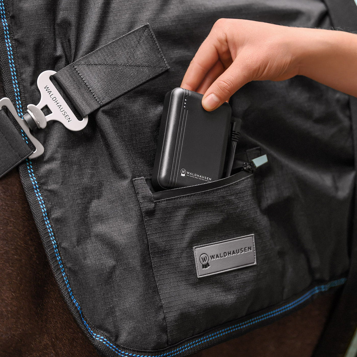 Einsetzen der originalen Waldhausen Powerbank (5000 mAh / 7,4 V) in die integrierte Reißverschlusstasche der Waldhausen TecSupreme Heiz- und Massagedecke am Pferd zur unterbrechungsfreien Stromversorgung der Wellness-Funktionen.