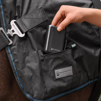 Einsetzen der originalen Waldhausen Powerbank (5000 mAh / 7,4 V) in die integrierte Reißverschlusstasche der Waldhausen TecSupreme Heiz- und Massagedecke am Pferd zur unterbrechungsfreien Stromversorgung der Wellness-Funktionen.