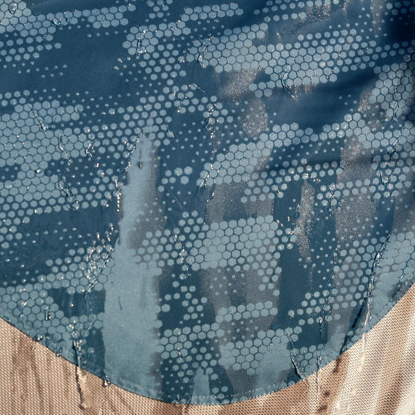 Eine Nahaufnahme der LeMieux Arika Camo Shower-Tek Hybriddecke zeigt kleine Wassertropfen auf dem oberen, wasserdichten Ripstop-Material, welches durch den Regen reagiert und seinen innovativen, wasserreaktiven Camouflage-Print im Farbton Jungle offenbart.