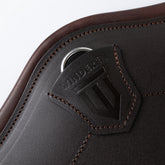 Detailaufnahme des Winderen-Dressursattelgurts in Braun aus der Pressure-Relief-Serie. Das hochwertige Vollnarbenleder mit feinen Ziernähten zeigt eine elegante Abdeckung mit geprägtem Winderen-Logo, welche den integrierten Karabinerhaken für Hilfszügel sicher und funktional verdeckt.