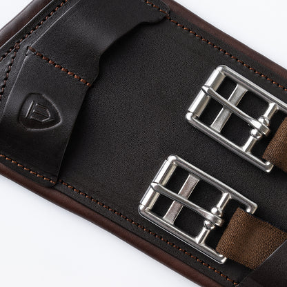 Nahaufnahme des Schnallenbereichs vom braunen Winderen-Dressursattelgurt aus Vollnarbenleder. Zu sehen sind zwei Edelstahl-Rollenschnallen mit braunen Elastikenden sowie eine flache Lederlasche mit der charakteristischen Winderen-Logo-Prägung, die für einen eleganten Sitz der Gurtstrippen sorgt.