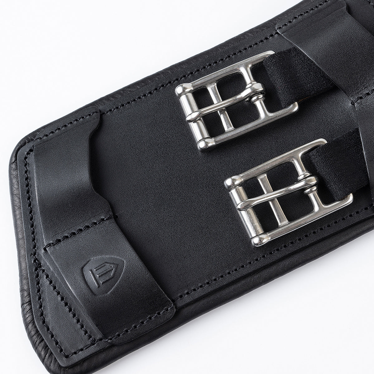 Detailansicht der Edelstahl-Rollenschnallen mit flachen Elasteinsätzen und der Lederlasche mit Winderen-Logo am schwarzen Pressure-Relief-Dressursattelgurt. Die elastischen Enden ermöglichen eine optimale Dehnung des Brustkorbs beim Reiten. Zusammen mit der weichen Unterpolsterung schützt dieser ergonomische Lederkurzgurt das Pferd vor Druckstellen und ist die ideale Wahl bei Gurtzwang sowie für empfindliche Pferde.