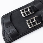 Detailansicht der Edelstahl-Rollenschnallen mit flachen Elasteinsätzen und der Lederlasche mit Winderen-Logo am schwarzen Pressure-Relief-Dressursattelgurt. Die elastischen Enden ermöglichen eine optimale Dehnung des Brustkorbs beim Reiten. Zusammen mit der weichen Unterpolsterung schützt dieser ergonomische Lederkurzgurt das Pferd vor Druckstellen und ist die ideale Wahl bei Gurtzwang sowie für empfindliche Pferde.