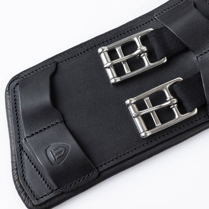 Detailansicht der Edelstahl-Rollenschnallen mit flachen Elasteinsätzen und der Lederlasche mit Winderen-Logo am schwarzen Pressure-Relief-Dressursattelgurt. Die elastischen Enden ermöglichen eine optimale Dehnung des Brustkorbs beim Reiten. Zusammen mit der weichen Unterpolsterung schützt dieser ergonomische Lederkurzgurt das Pferd vor Druckstellen und ist die ideale Wahl bei Gurtzwang sowie für empfindliche Pferde.
