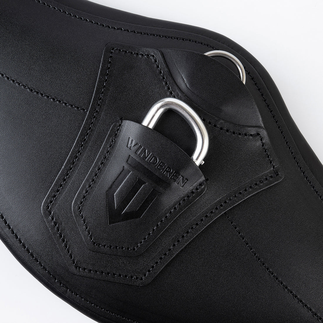 Nahaufnahme des Winderen Sattelgurtes mit kleinem Bauchlatz in Schwarz. Gezeigt wird die Abdeckung mit eingeprägtem Logo über dem halb versenkten Karabiner für Vorderzeuge sowie der darüber liegende D-Ring für Hilfszügel.