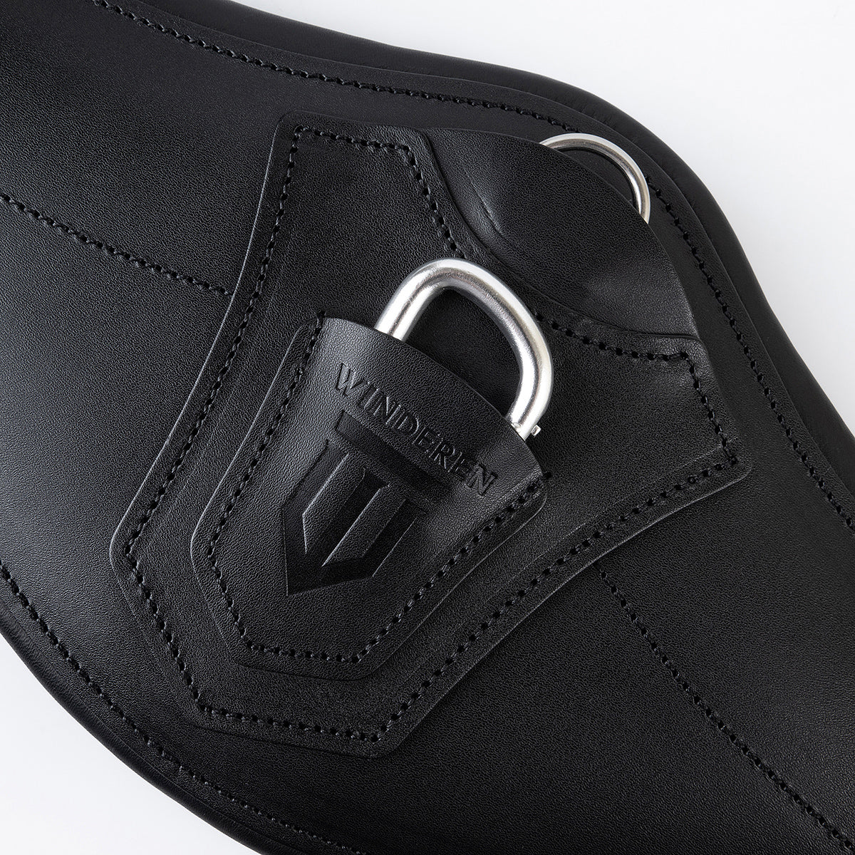 Nahaufnahme des Winderen Sattelgurtes mit kleinem Bauchlatz in Schwarz. Gezeigt wird die Abdeckung mit eingeprägtem Logo über dem halb versenkten Karabiner für Vorderzeuge sowie der darüber liegende D-Ring für Hilfszügel.
