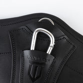 Makro-Nahaufnahme des schwarzen Winderen-Pressure-Relief-Springgurtes mit kleinem Bauchlatz aus Vollnarbenleder. Die Detailansicht zeigt das tief eingeprägte Winderen-Logo auf der Leder-Schutzlasche, den halb versenkten Aluminium-Karabiner zur Befestigung von Vorderzeugen, den darüber liegenden Edelstahl-D-Ring für Hilfszügel sowie die präzisen Tonnähte.