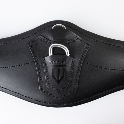 Detailansicht des schwarzen Winderen Pressure-Relief Springgurtes mit kleinem Bauchlatz aus hochwertigem Vollnarbenleder. Die Nahaufnahme zeigt die Leder-Schutzabdeckung mit geprägtem Winderen-Logo über dem halb versenkten Aluminium-Karabiner für das Einhaken von Vorderzeugen sowie den darüber liegenden Edelstahl-D-Ring für Hilfszügel wie Martingale.
