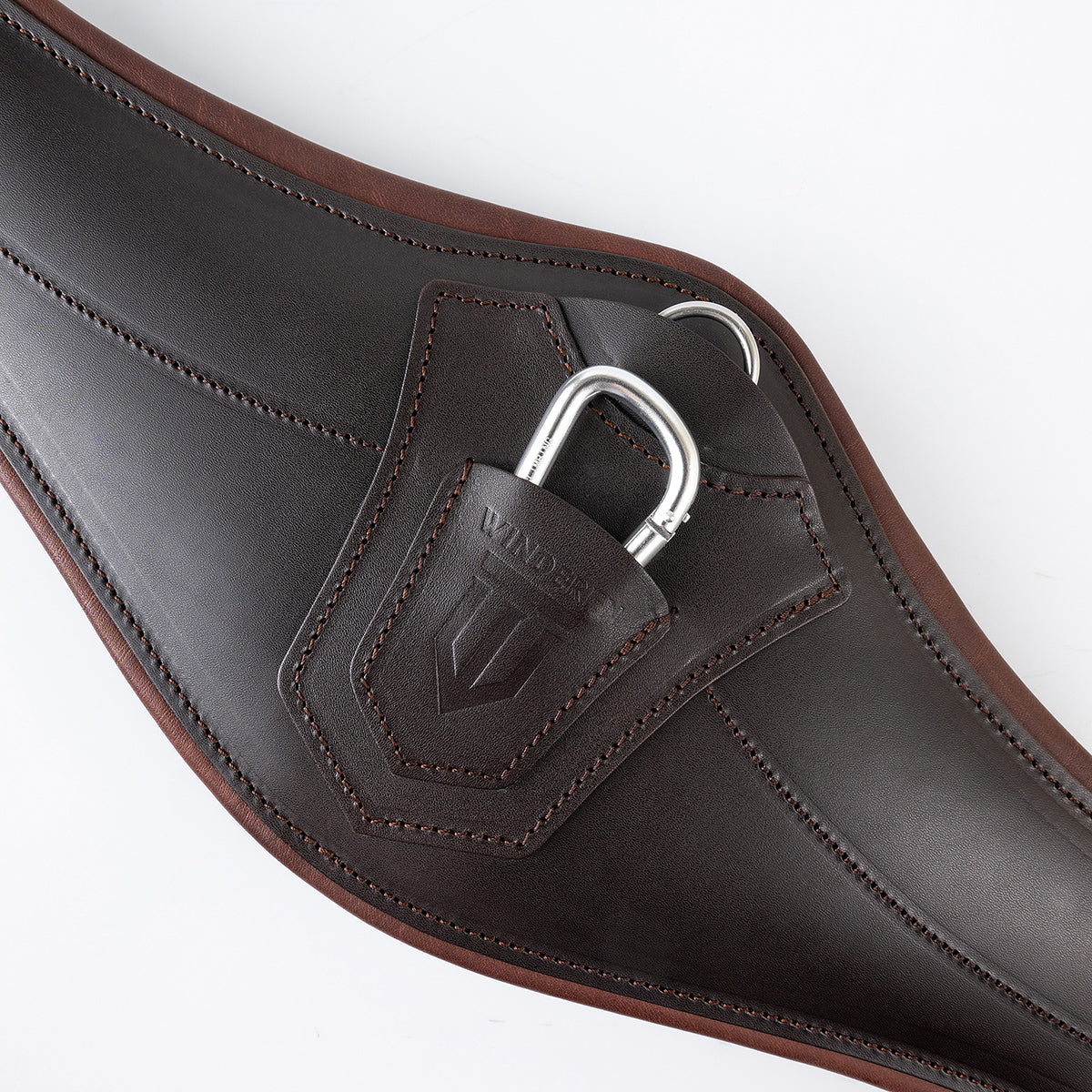 Zentralansicht des braunen Winderen Pressure-Relief Springgurts mit kleinem Bauchlatz. Die Aufnahme zeigt den anatomisch geformten Stoßschutz aus Vollnarbenleder mit halb versenktem Aluminium-Karabiner und zweifarbiger Polsterung für optimale Bewegungsfreiheit beim Springen ohne Stollen.
