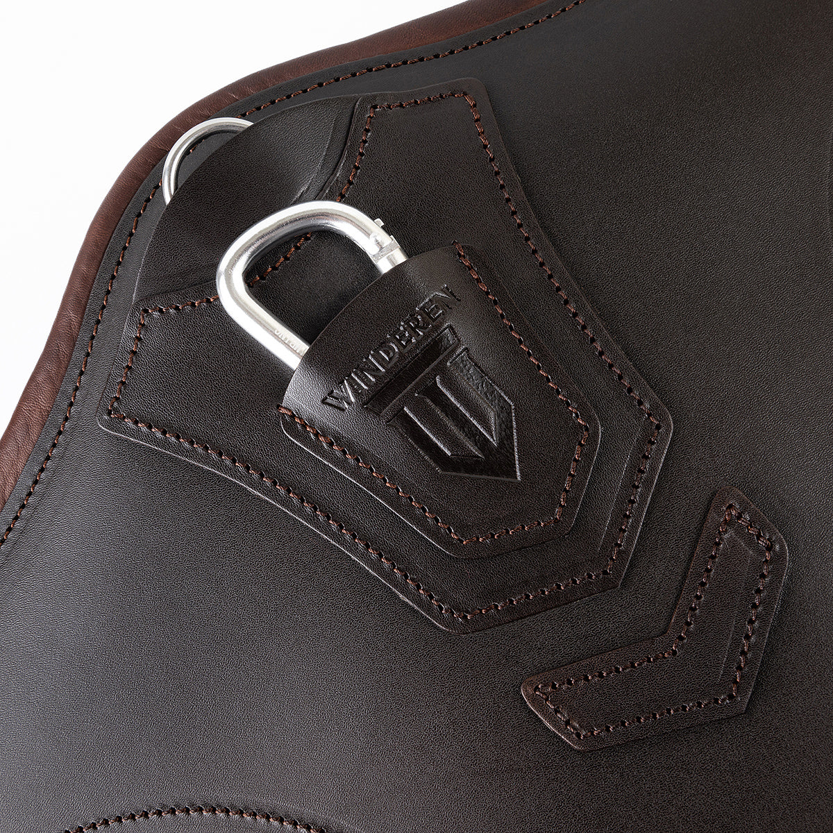 Detailaufnahme des braunen Winderen-Pressure-Relief-Stollengurts aus Vollnarbenleder mit eingeprägtem Winderen-Logo. Zu sehen sind der halb versenkte Aluminium-Karabiner unter einer Schutzabdeckung aus Leder zum sicheren Einhaken des Vorderzeugs sowie der darüber liegende D-Ring für Hilfszügel wie das Martingal. Die präzisen Nähte und die flache Lederverarbeitung verhindern das Verfangen über dem Sprung. Perfekt durchdachtes Premium-Sattelzubehör für das Springreiten.