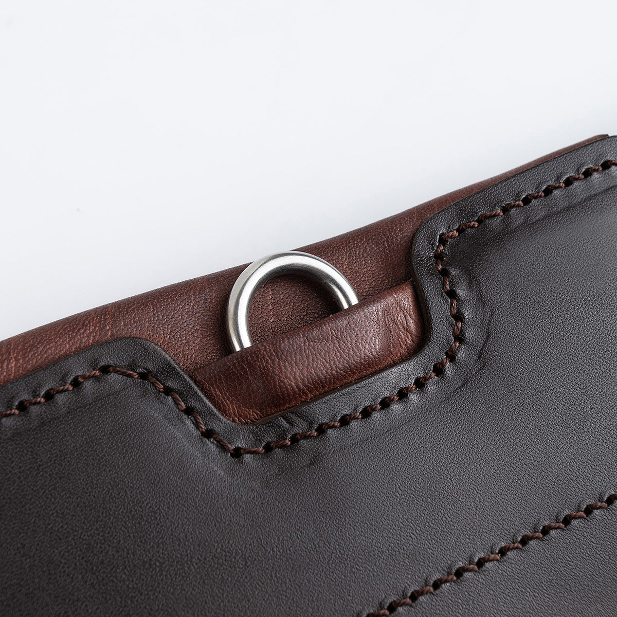 Detailaufnahme des seitlichen D-Rings unter einer flachen Lederabdeckung am braunen Winderen Pressure Relief Stollengurt. Der robuste D-Ring dient zur sicheren und schnellen Befestigung von Vorderzeugen und Hilfszügeln, ohne am Pferdekörper oder den Beinen zu reiben. Gut erkennbar sind die präzise Verarbeitung aus zweifarbigem Vollnarbenleder, die tonalen Nähte sowie die weiche rötlich-braune Kantenpolsterung. Durchdachtes Sicherheits-Feature für das Springreiten und Turniereinsätze.