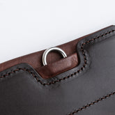 Detailaufnahme des seitlichen D-Rings unter einer flachen Lederabdeckung am braunen Winderen Pressure Relief Stollengurt. Der robuste D-Ring dient zur sicheren und schnellen Befestigung von Vorderzeugen und Hilfszügeln, ohne am Pferdekörper oder den Beinen zu reiben. Gut erkennbar sind die präzise Verarbeitung aus zweifarbigem Vollnarbenleder, die tonalen Nähte sowie die weiche rötlich-braune Kantenpolsterung. Durchdachtes Sicherheits-Feature für das Springreiten und Turniereinsätze.