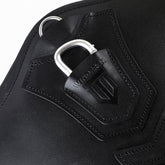 Makro-Detailansicht des schwarzen Winderen Pressure-Relief Stollengurts aus hochwertigem Vollnarbenleder. Die Nahaufnahme zeigt den unter einer edlen Lederlasche mit Winderen-Logoprägung halb versenkten Karabiner aus Aluminium zur Befestigung von Vorderzeugen sowie den halb versenkten D-Ring für Hilfszügel wie z. B. ein Martingal.