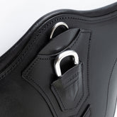Perspektivische Detailaufnahme der zentralen Bauchplatte des schwarzen Winderen Pressure-Relief Stollengurts aus Vollnarbenleder. Die Ansicht zeigt den halb versenkten Aluminium-Karabiner unter der geprägten Lederabdeckung für das schnelle Einhaken von Vorderzeugen ohne Verfangen sowie den flach integrierten D-Ring für Hilfszügel wie ein Martingal.