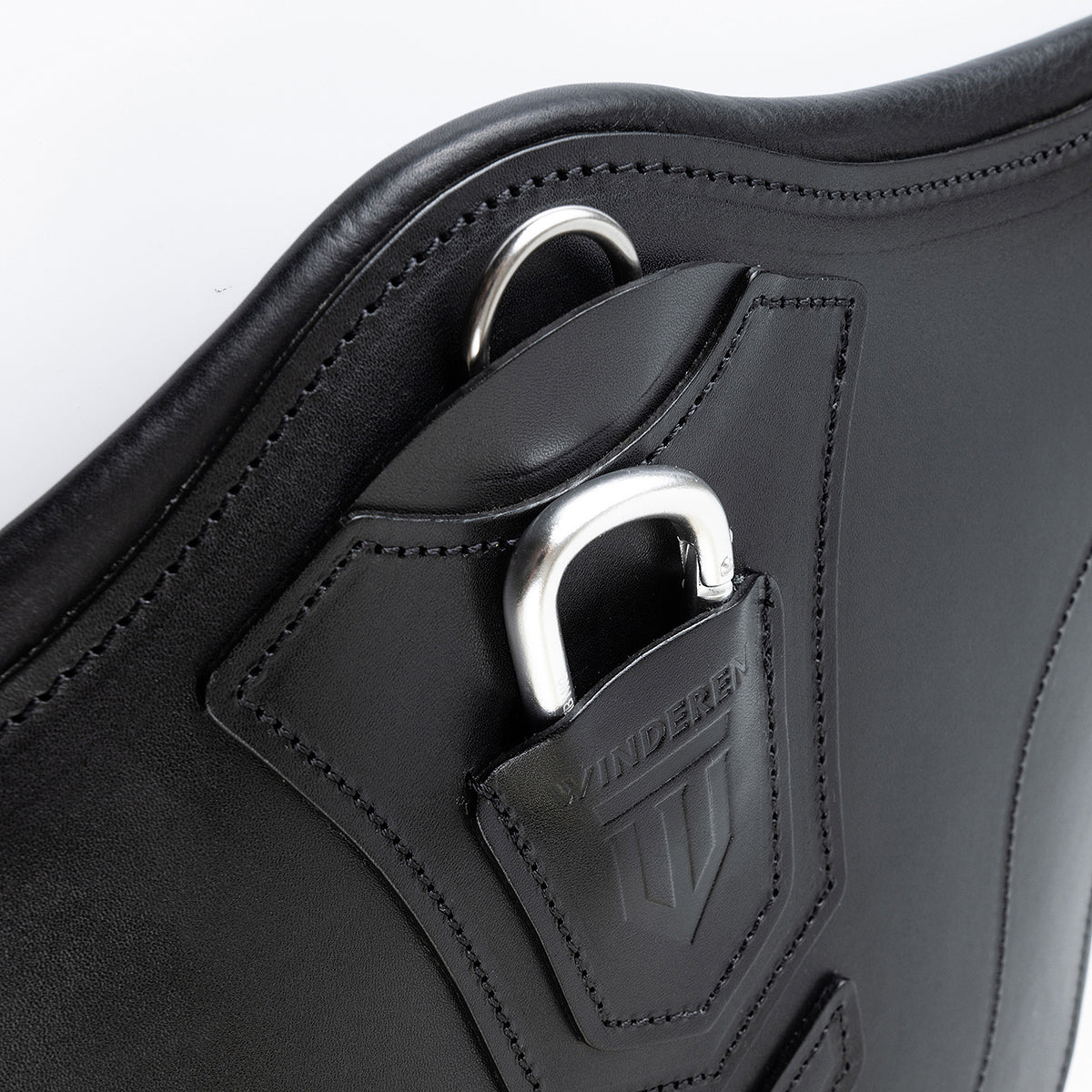 Perspektivische Detailaufnahme der zentralen Bauchplatte des schwarzen Winderen Pressure-Relief Stollengurts aus Vollnarbenleder. Die Ansicht zeigt den halb versenkten Aluminium-Karabiner unter der geprägten Lederabdeckung für das schnelle Einhaken von Vorderzeugen ohne Verfangen sowie den flach integrierten D-Ring für Hilfszügel wie ein Martingal.